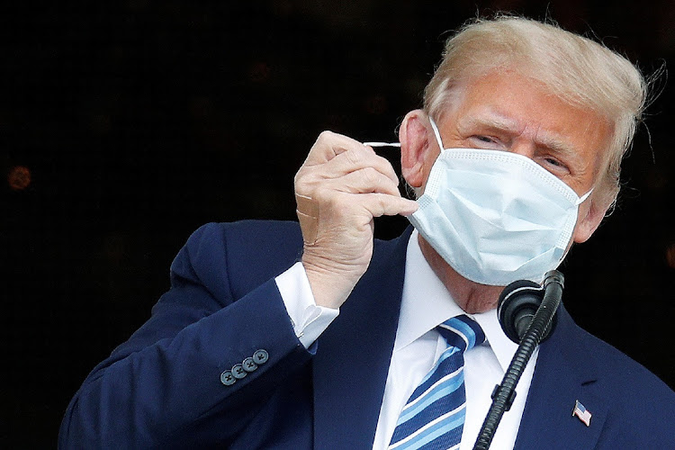 U.S. President Donald Trump, with bandages seen on his hand, takes off his face mask as he comes out on a White House balcony to speak to supporters gathered on the South Lawn for a campaign rally in Washington, U.S., October 10, 2020.
