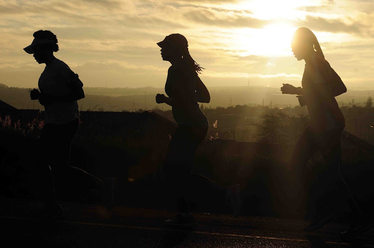 A group of social runners training for a marathon running in Olievenhoutbosch towards Centurion silhouetted by an early morning sunrise.