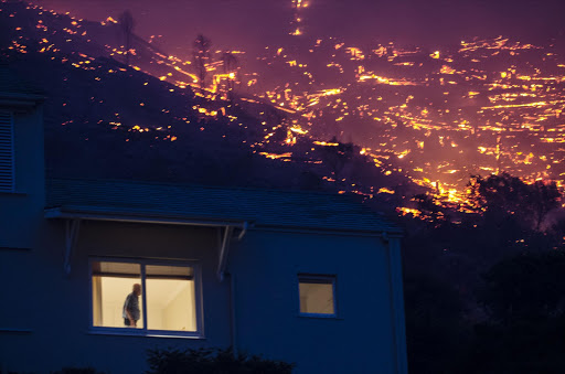 A man is seen in the window of a home surrounded by the embers of the Simon's Town fire.