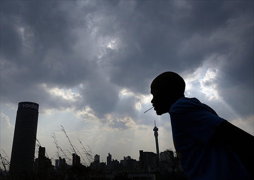 A man walks past the Johannesburg skyline as ominous storm clouds hang overhead on 8 October 2007. load shedding. Eskom. Power outage. storm.