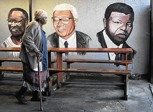 ESTEEMED COMPANY: Sarah Kunene, 84, walks past a mural depicting ANC leaders Oliver Tambo, Walter Sisulu and former president Nelson Mandela at a spaza shop in Soweto yesterday. Mandela is undergoing medical tests