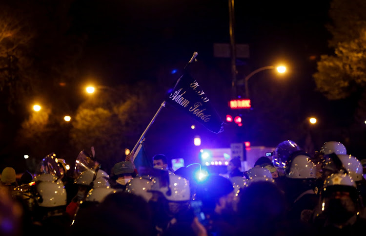 A protester waves a flag as Chicago Police Department officers secure during a demonstration, a day after officials released a graphic body-camera video showing a police officer shooting and killing 13-year-old boy Adam Toledo two weeks ago while he appeared to be raising his hands.