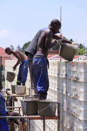 Community members fill plastic formwork with concrete and a Moladi additive during the construction of a house.