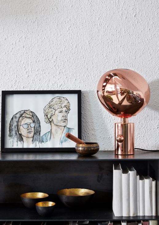 An illustrated image of Craig and Christian, a Copper Melt table lamp by Tom Dixon, porcelain 'books' and a textured wall catch light coming down from skylight.