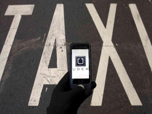 The logo of car-sharing service app Uber on a smartphone over a reserved lane for taxis in a street is seen in this December 10, 2014 file photo illustration. REUTERS/Sergio Perez