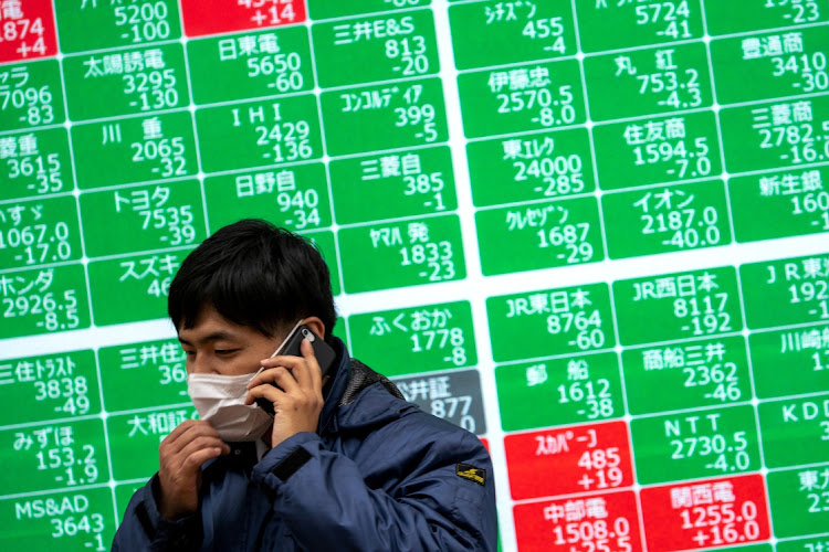 A man wearing a protective face mask talks on his cellphone in front of a screen showing the Nikkei index outside a brokerage in Tokyo, Japan. Picture: REUTERS/ATHIT PERAWONGMETHA