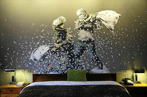 The rooms in the Walled Off hotel in Bethlehem invite guests to sleep inside works of art. This one features a Banksy wall painting of an Israeli border policeman and Palestinian in a pillow fight.