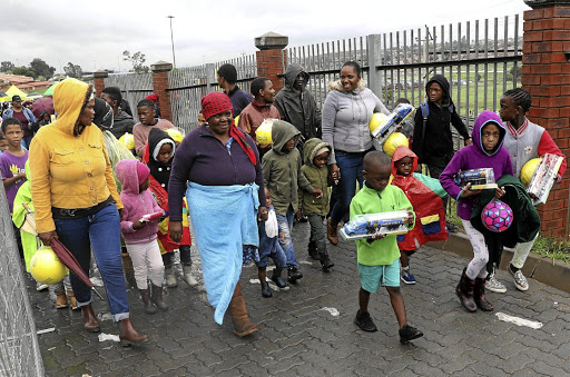 Some of the children who braved the cold and rainy weather walk alongside their parents and guardians after receiving their toys from the Motsepe Foundation at Orlando Stadium in Soweto yesterday.