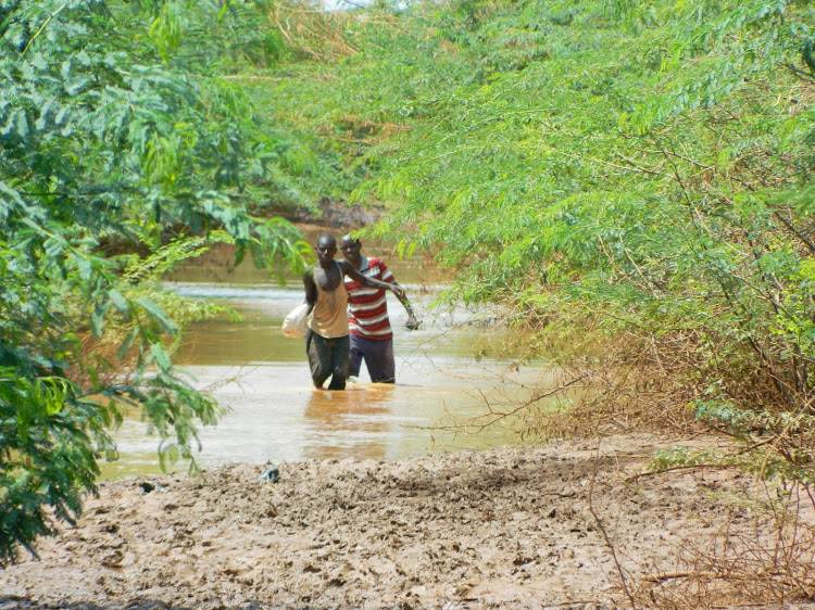 Farmers wade through a flooded farm in Garissa
