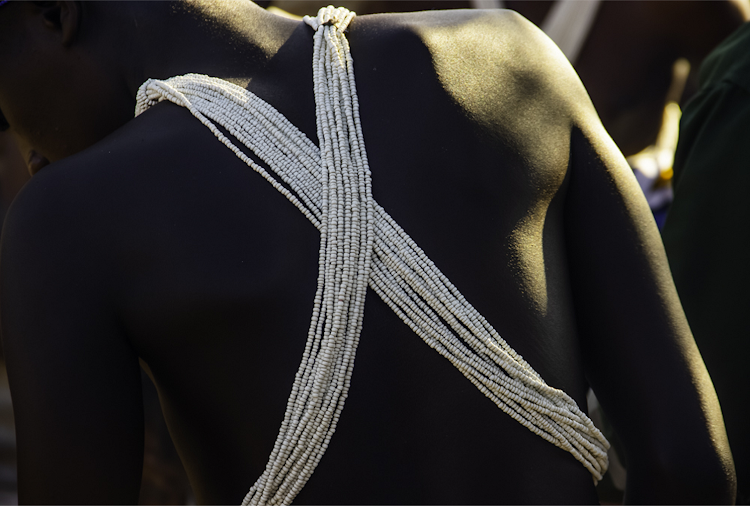 The white cross-body beadwork that identifies the wearer as a returned initiate. When they leave, they wear only the loincloth, a different stick and a grass ball on their foreheads.