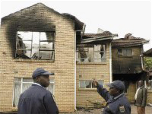 DEATH BY FIRE: Limpopo businessman Elliot Thanyani and police survey the damage to his 15-roomed double-storey house, which burnt at the weekend killing his two daughters. PIc. Elmon Tshikudo.