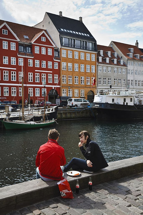 Couple having lunch outdoors on the quayside at new harbour, Nyhavn, Copenhagen, Denmark.