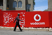 A pedestrian walks past a Vodacom-branded billboard.