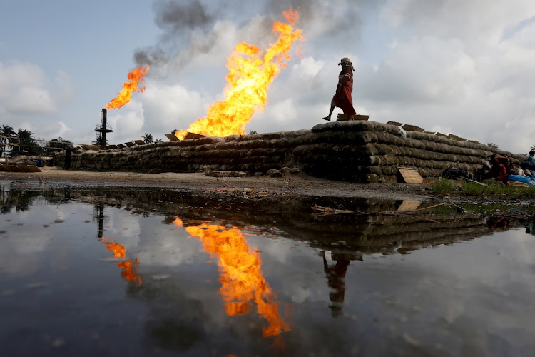 Two gas flaring furnaces and a woman walking on sand barriers are reflected in the pool of oil-smeared water at a flow station in Ughelli, Nigeria. File photo.