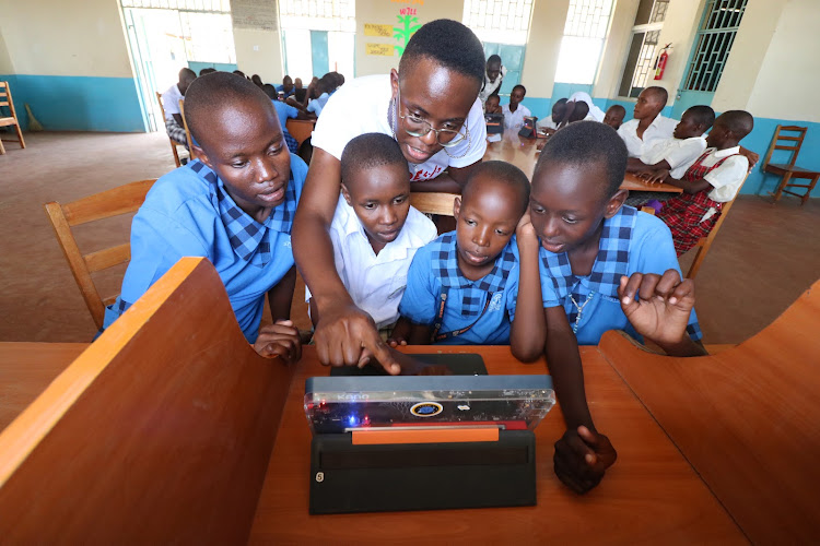 A teacher instructs pupils how to operate a laptop.