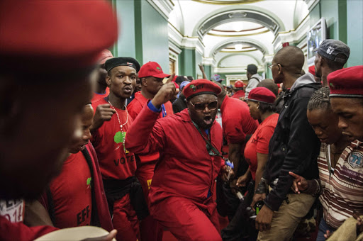 File photo: Economic Freedom Fighters (EFF) members chant slogans as they storm the Gauteng Legislature building after a march over a ruling against the wearing of red overalls in the Gauteng Legislature assembly. Photo credit: AFP