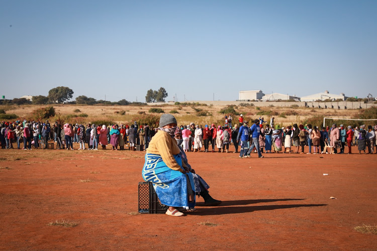 A woman rests on a crate as hundreds of people queue to collect food parcels in Iterileng, Pretoria.