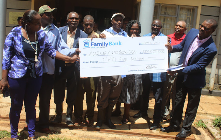 Beneficiaries of Gichugu NG-CDF bursary cheques pose for a photo with a dummy cheque with their MP Gichimu Githinji at the NG-CDF offices in Kianyaga in Gichugu constituent Monday