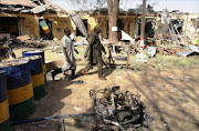 Two residents pass by bombed corner shops attached to Bompai police barracks in the northern Nigerian city of Kano on January 24, 2012, after multiple explosions and gun assaults by Boko haram Islamists on security formations in the city killed 185 people.
