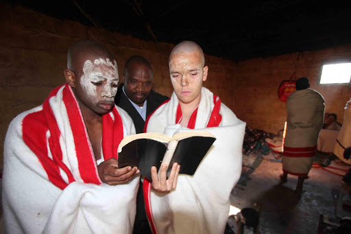 RESPECT: Hudson Park Grade 11 pupils Estiaan Swanepoel, his longtime friend, classmate and fellow initiate Ndibulele Sobhoyisi and their traditional surgeon Phinda Malova reading a Holy Bible at the initiation school run by Malova in Centane . Picture:LULAMILE FENI