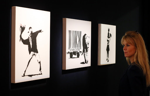 Employee Leonora Oldfield looks at Banksy's (L-R) 'Love is in the Air', 'Leopard and Barcode' and 'Bomb Hugger' at Bonhams auctioneers on March 23, 2012 in London, England. The paintings form part of the Urban Art Sale, which takes place at Bonhams on March 29, 2012.