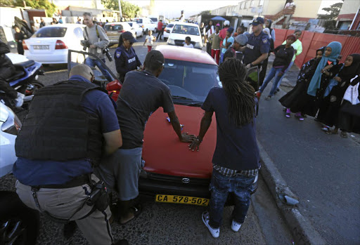 An officer searches men in Parkwood on the Cape Flats on Wednesday, when Cape Town Metro Police conducted operations in the area.