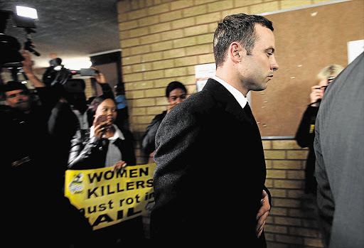 TOUGH DAY: Oscar Pistorius leaves the Pretoria High Court after a day of testimony in which the impact of law-enforcement calibre bullets was described. An ANC Women's League protester is the background