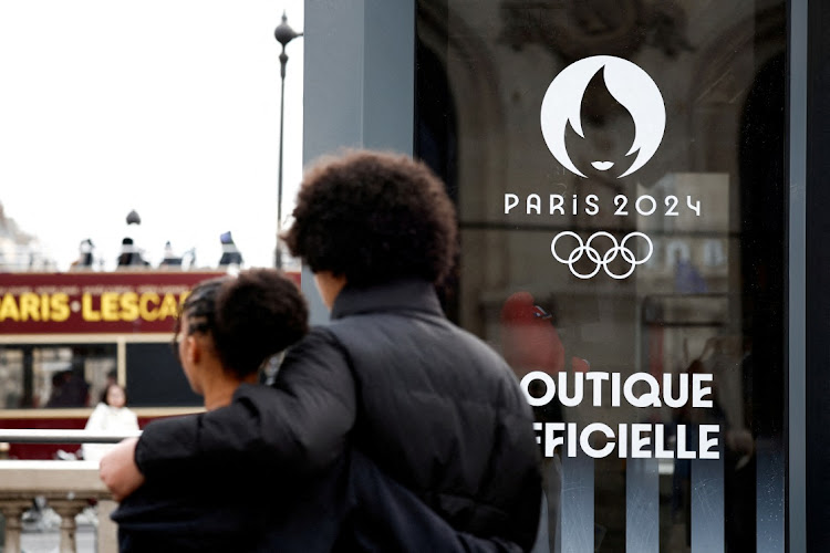 People walk near the logo of the Paris 2024 Olympic and Paralympic Games on an official Paris 2024 store at Place de l'Opera in Paris, France, January 1, 2024.