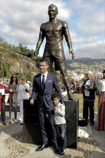 Portuguese football player Cristiano Ronaldo from the Real Madrid poses with his son beneath a statue of himself during the unveling ceremony in his hometown in Funchal on December 21, 2014. AFP PHOTO / GREGORIO CUNHA