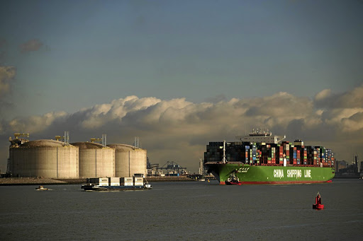 A container ship is guided into the port of Rotterdam as liquid natural gas storage silos stand on the shore. PICTURE: JASPER JUINEN/BLOOMBERG