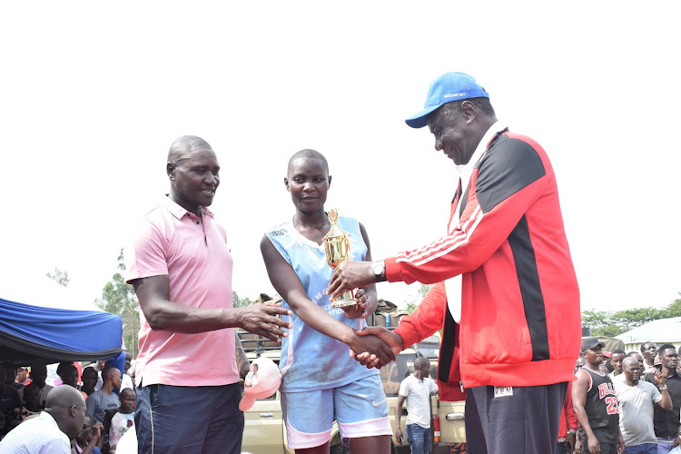 KVF President Charles Nyaberi hands a trophy to Bishop Sulumeti Girls captain after the conclusion of Arthur Odera Open Volleyball Tournament at Malaba Stadium on Sunday.