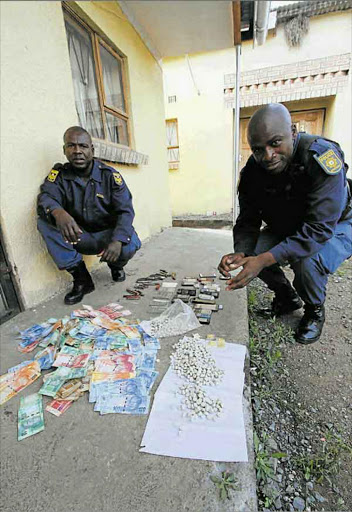 CLAMPING DOWN: Mthatha K9 police unit officers Sergeant Litha Ngxukumeshe and Constable Litha Sidwangube with the recovered items of cash, cellphones and ID books found by police at Chris Hani informal settlement near Mthatha yesterday Picture: LULAMILE FENI