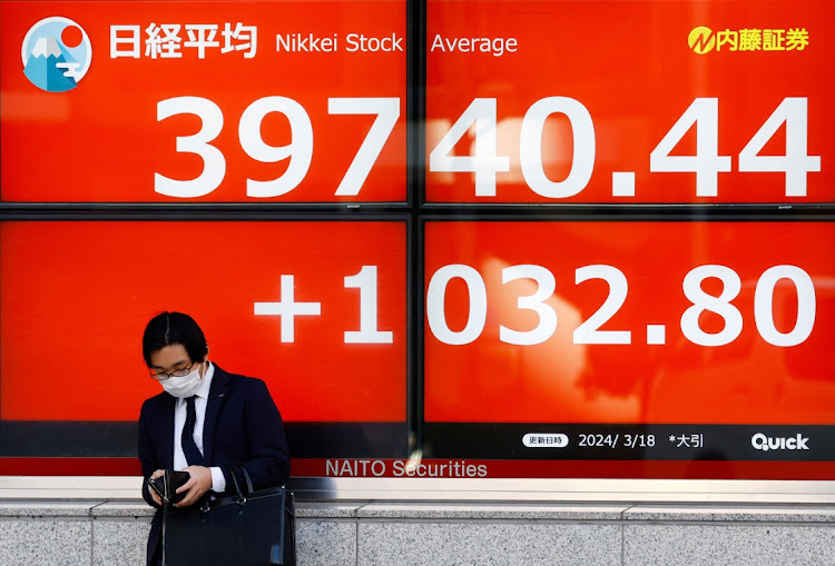 A man looks at his purse in front of an electronic screen displaying Japan’s Nikkei share average outside a brokerage in Tokyo, Japan, on March 18 2024. Picture: REUTERS/KIM KYUNG-HOON