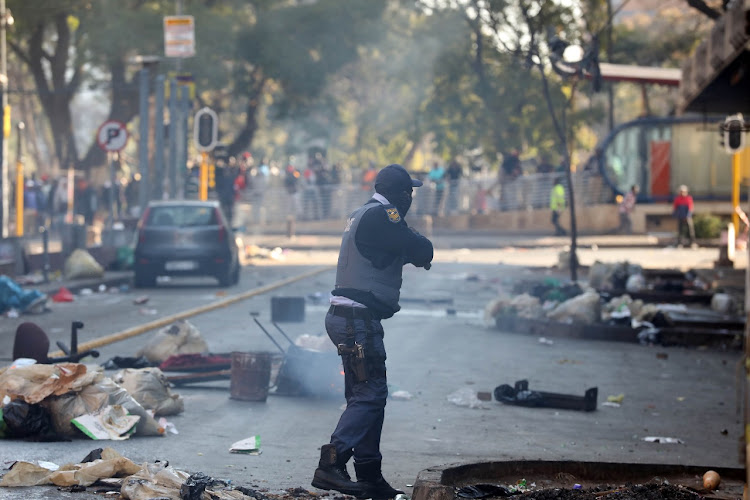 A police officer stands in a debris-strewn Jules Street in Malvern, Johannesburg, on Sunday. Protests that started in KwaZulu-Natal following the imprisonment of former president Jacob Zuma moved to Gauteng late on Saturday night and continued into Sunday.