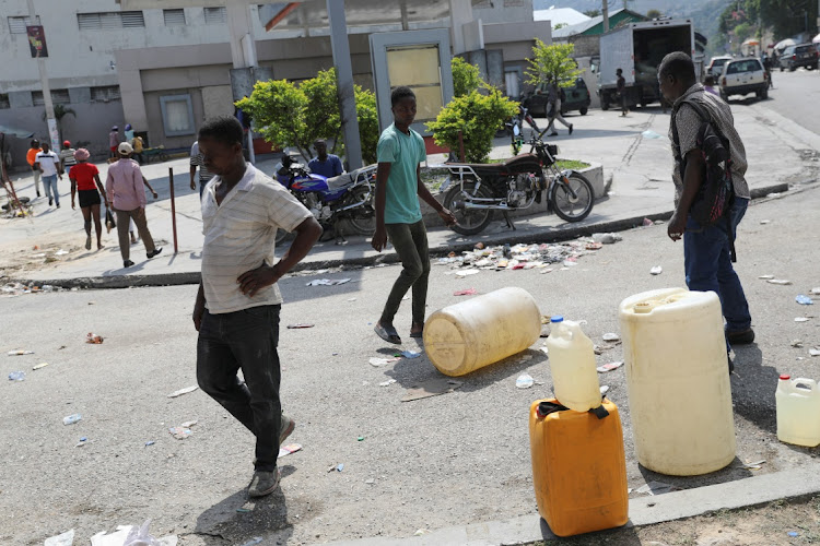 People walk by plastic containers outside a petrol station during a fuel shortage as the government said it would extend a state of emergency for another month after an escalation in violence from gangs seeking to oust the Prime Minister Ariel Henry, in Port-au-Prince, Haiti, March 7, 2024.