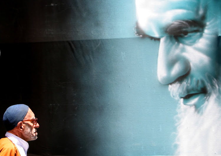 A man walks past a poster of Ayatollah Ruhollah Khomeini.