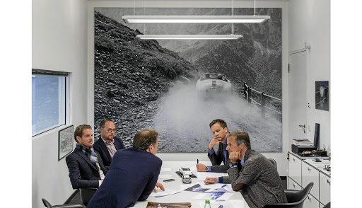 Porsche designers sit in an office with a picture that shows how the brand’s DNA was born with a classic 356 on a mountain road in the 1950s