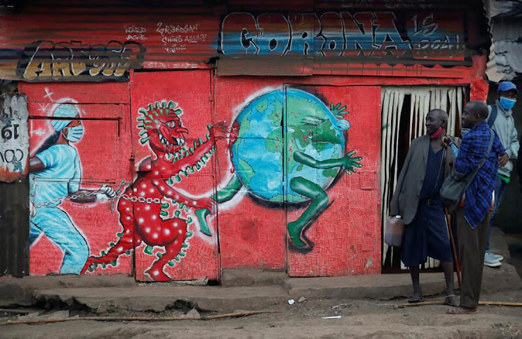 Vendors carrying traditional medicine in jerrycans, stand outside a stall which has graffiti against the spread of the coronavirus disease (COVID-19) within Kibera slums in Nairobi, Kenya.