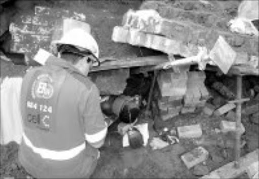 TRAPPED: A member of the emergency rescue services tries to remove one of the two construction workers who were trapped under rubble when a wall of a building collapsed in Merewent, south of Durban. Pic. ER24.