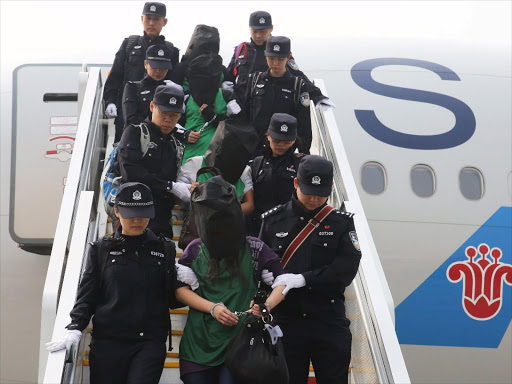 Police escort a group of people wanted for suspected fraud in China, after they were deported from Kenya, as they get off a plane after arriving at Beijing Capital International Airport in Beijing, China, April 13, 2016. Photo/REUTERS