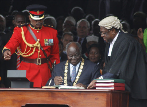 President Mwai Kibaki signs the documents of the new constitution as AG Amos Wako looks on at Uhuru Park during the promulgation of the new constitution on August 27, 2010
