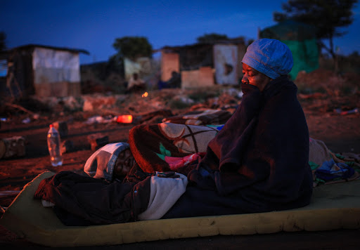 A 62-year-old woman tries to keep warm after her shack was demolished on November 22, 2014 in Pretoria, South Africa. The "Red Ants' demolished shacks which were put up on the council-owned land in Nellmapius. The settlement known as 'Malemaville" was established by Economic Freedom Front activists. File photo.