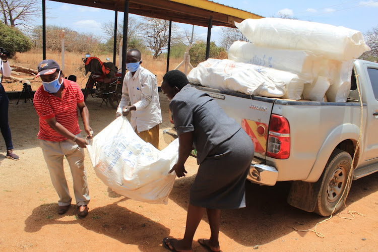 Kitui value chain specialist,[in red t-shirt] helps Ngomeni beekeepers offload bee harvesting materials in Ngomeni town.
