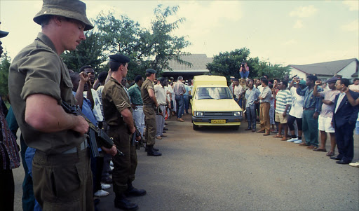 Soldiers line the road outside Chris Hani's home in Dawn Park, Boksburg as a police van prepares to take the body of the South African Communist Leader away on 10 April 1993.