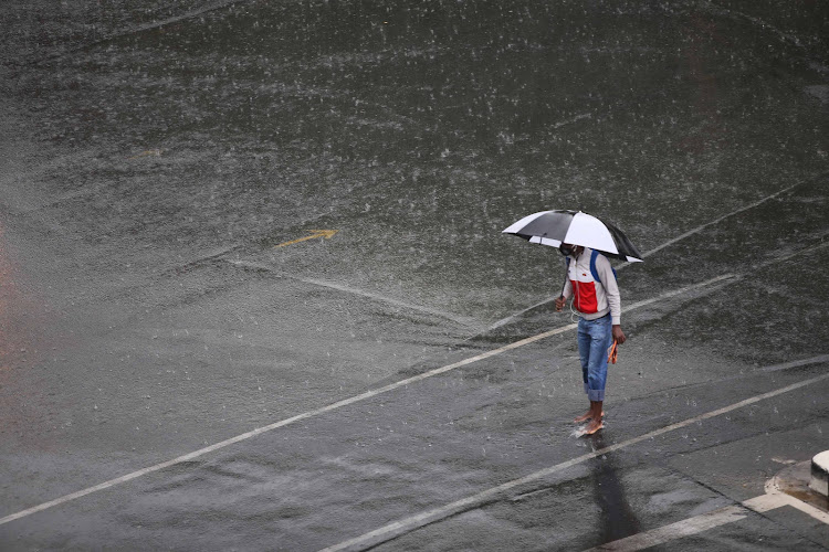 A man carries his sandals as he crosses a street during a rainy day in Johannesburg yesterday.