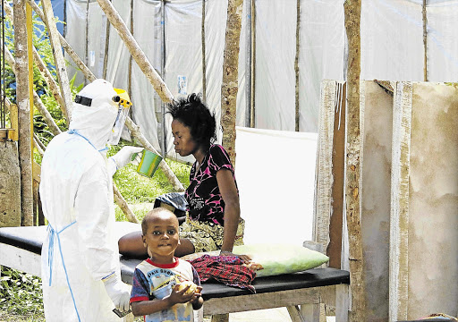 MASKED MERCY: A health worker in protective gear offers water to a woman with the Ebola virus disease at a treatment centre in Kenema, Sierra Leone, this week