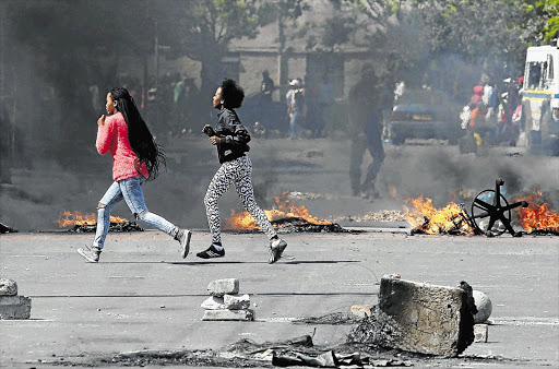 NOT THEIR SCENE: Girls run for cover after Langa residents barricaded a road during a service delivery protest yesterday.