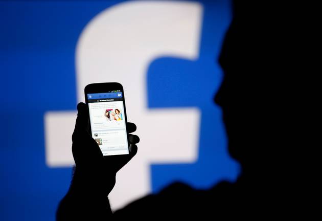 A man is silhouetted against a video screen with an Facebook logo.