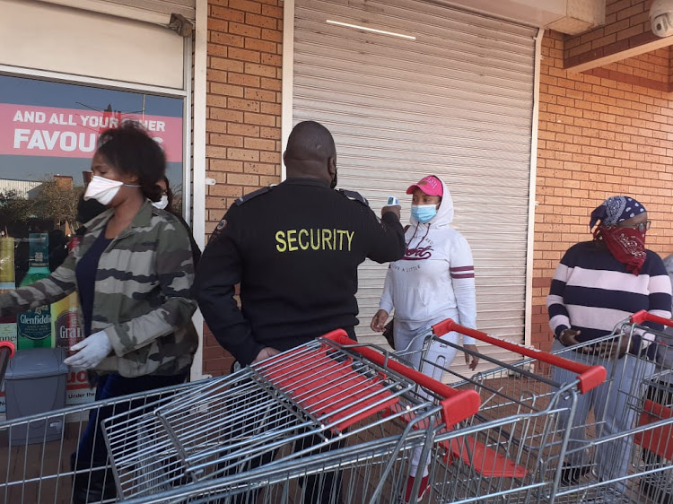 A security guard performs a temperature check outside a Gauteng liquor outlet on Monday, as queues form on the first day of booze sales being allowed again.