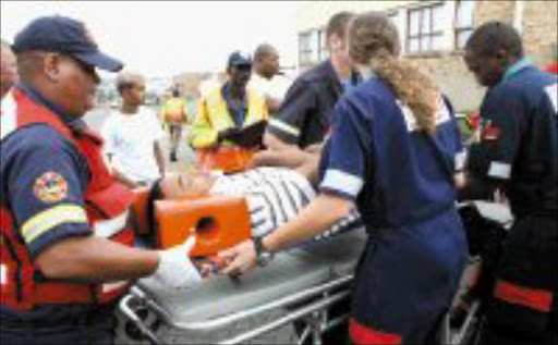 LIFE SAVERS: Alistair Hoffman, 18, is taken unconscious from his bakkie after the vehicle he was driving collided with a stationary vehicle in Industria, west of Johannesburg, yesterday. Pic. Lucky Nxumalo. © Sowetan.